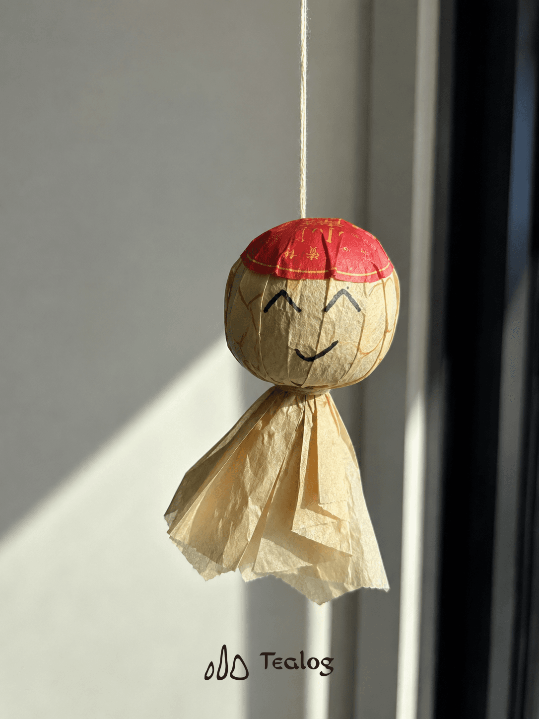 A Tangerine Pu-erh made into a smiling sunny-day doll, hanging in a sunlit window